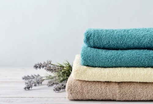 Stack,Of,Bath,Towels,With,Lavender,Flowers,On,Light,Wooden