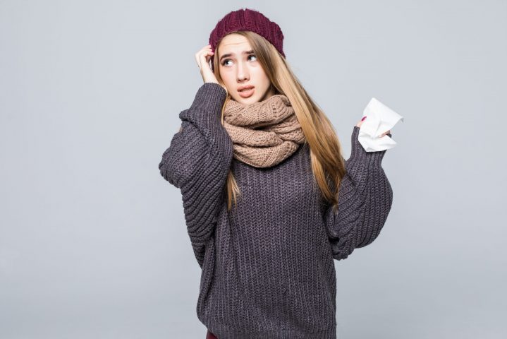 Pretty girl in grey sweater is cold isolated on gray